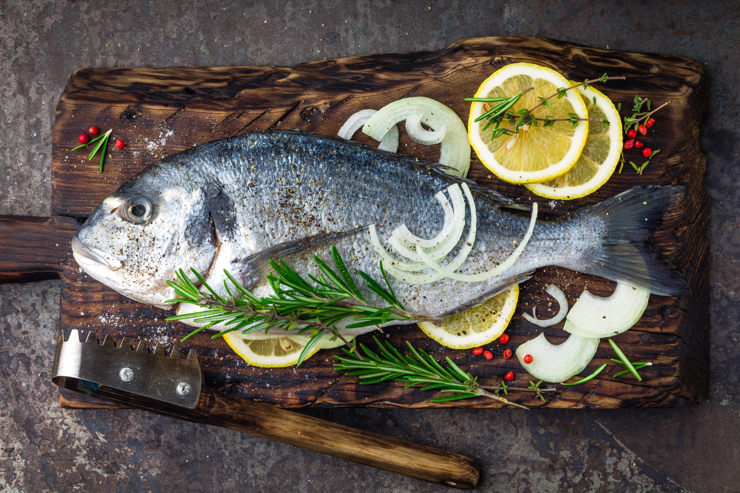 poisson cru sur planche avec aromates, oignon coupé et tranches de citron