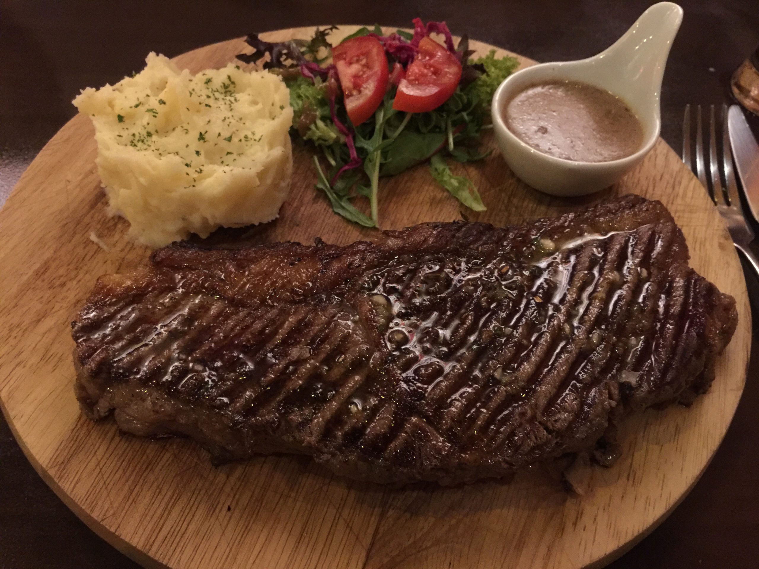 steak sur assiette en bois avec salade, sauce poivre et purée maison